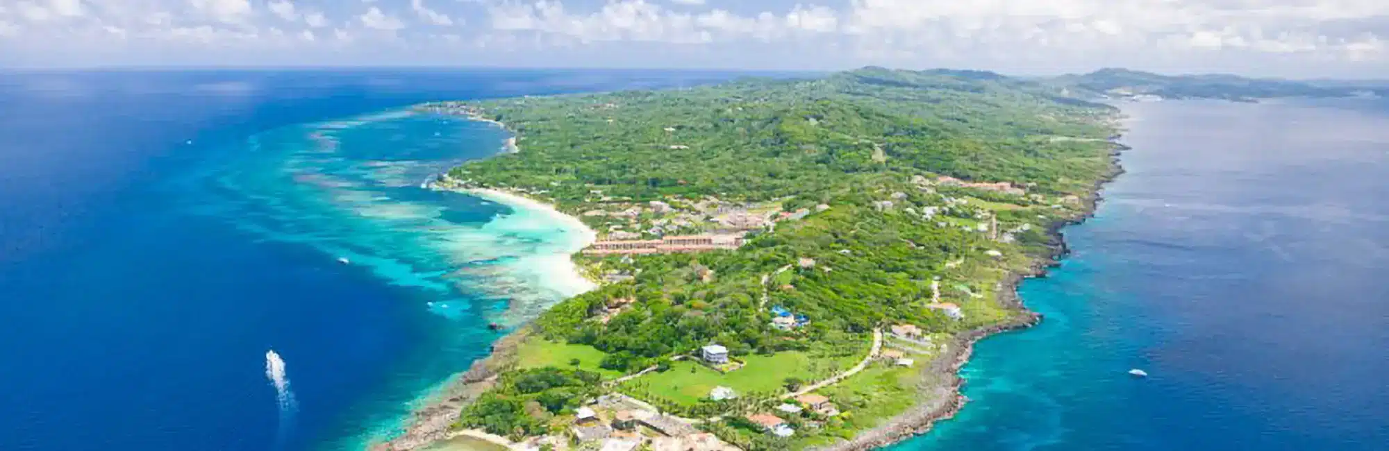 Aerial panorama of Roatan’s West Bay: turquoise reefs, white sands, lush greenery, and clear Caribbean waters ideal for PADI IDC course in Roatan.