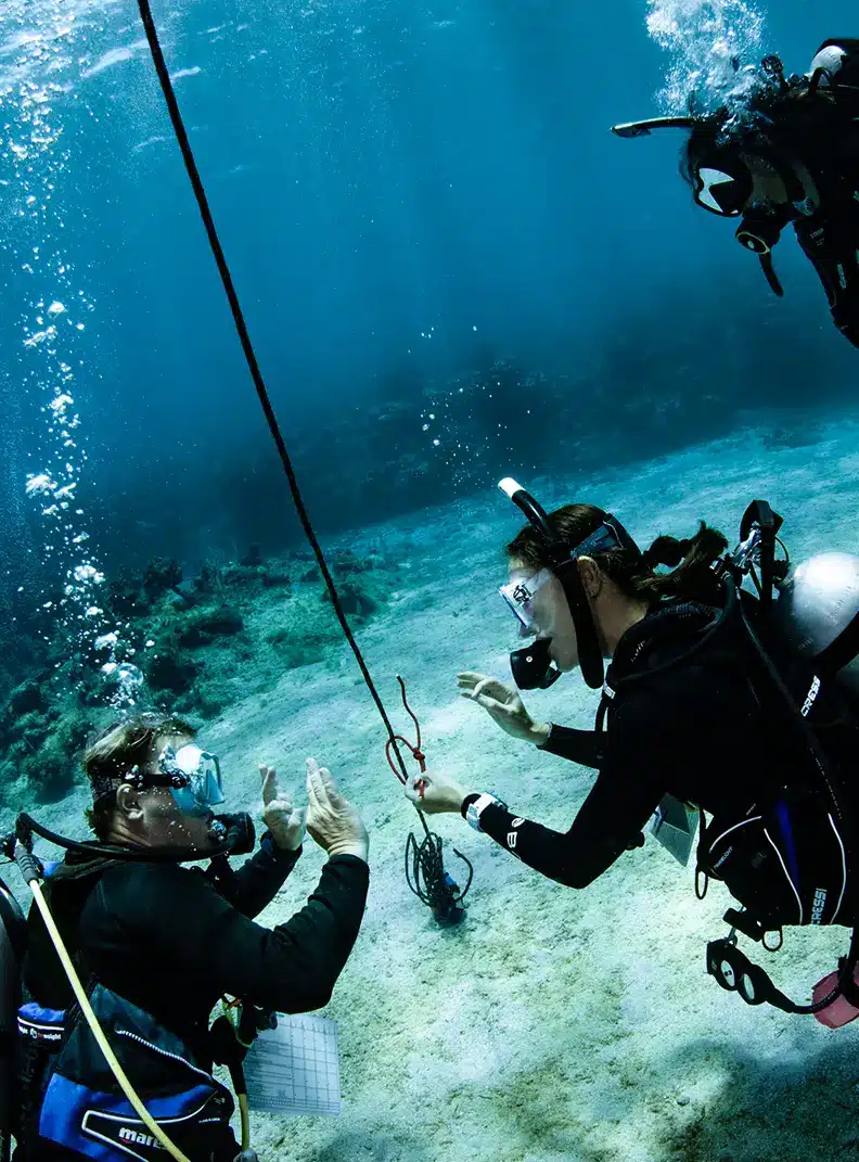PADI Course Director instructing IDC candidate on knot-tying underwater in Roatan’s clear blue waters, practicing rescue skills on sandy bottom.